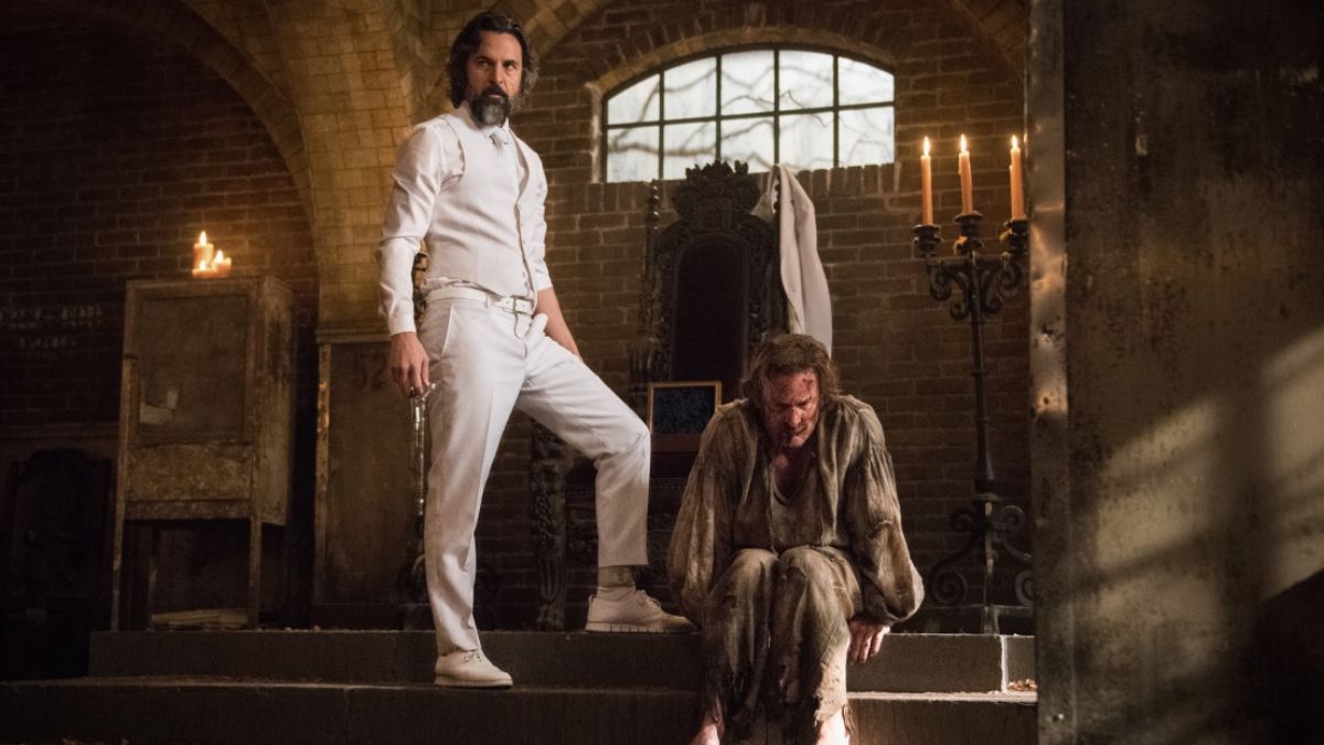 Jeffrey Vincent Parise as Asmodeus stands with Richard Speight Jr as Gabrielm sitting at his feet in Supernatural