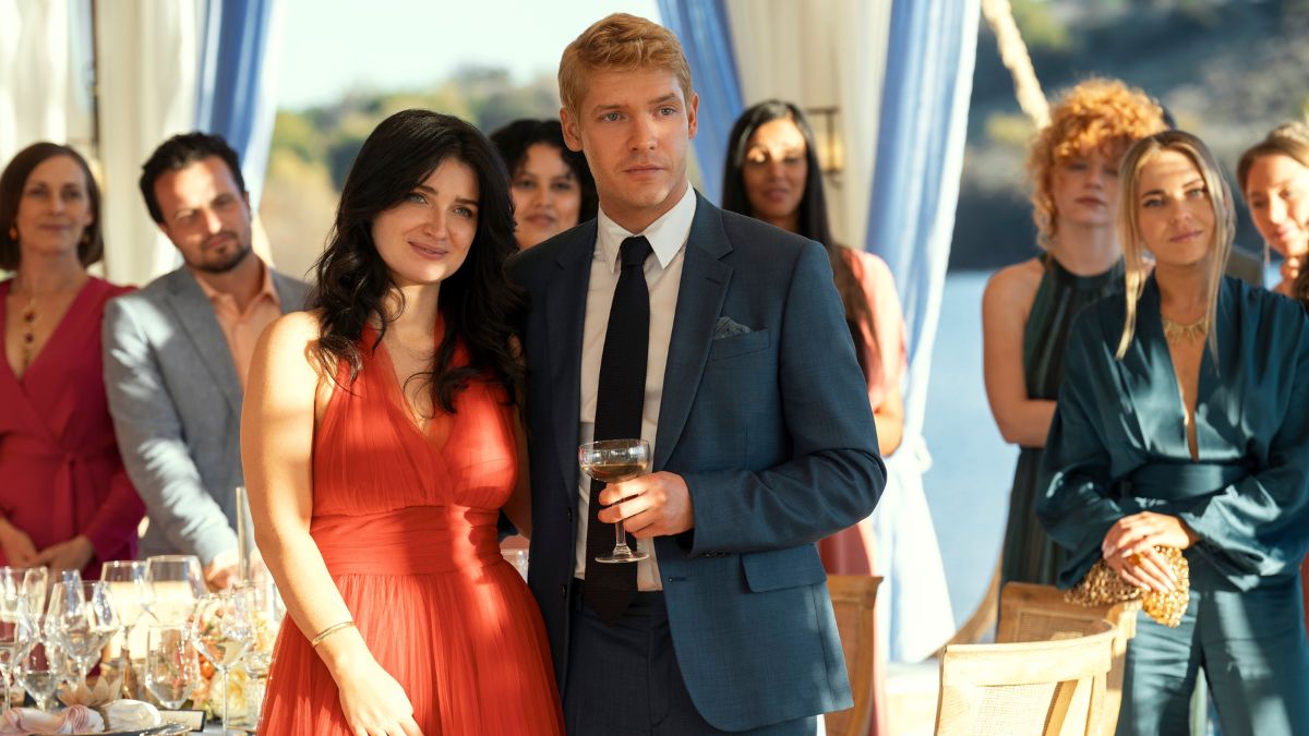 Eve Hewson as Amelia Sacks and Billy Howle as Benji Winbury watch someone giving a toast in The Perfect Couple