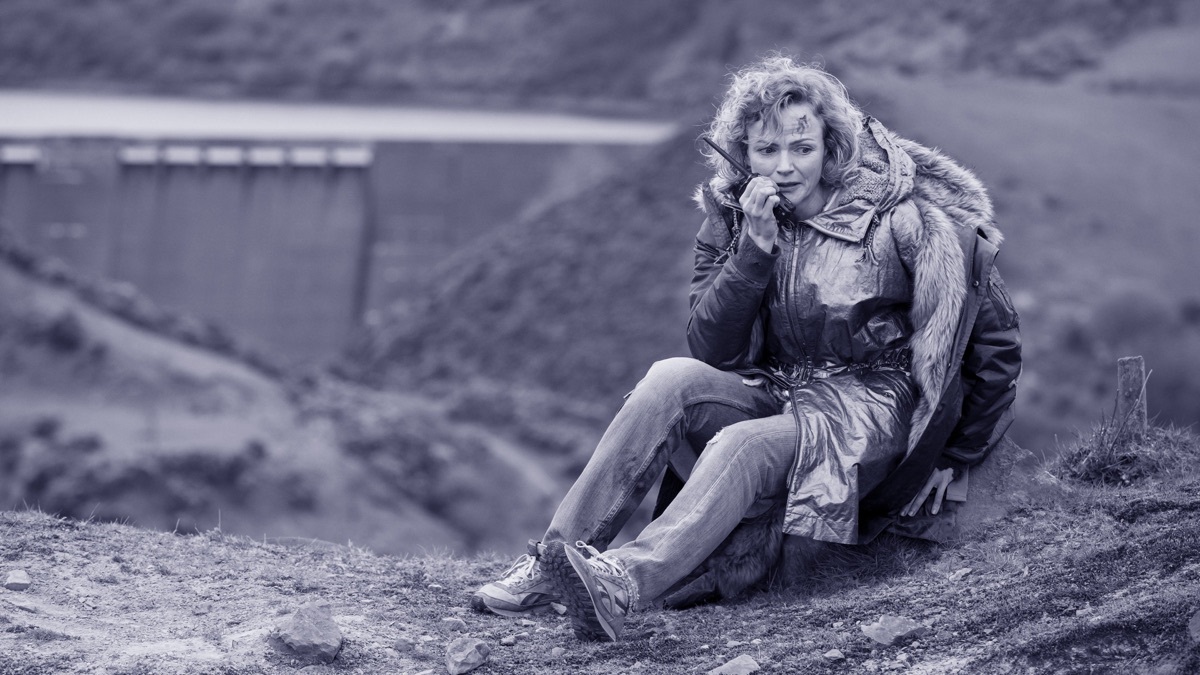 A woman sits with her hand pressed to her cheek, holding a walkie-talkie in 'Black Mirror' 