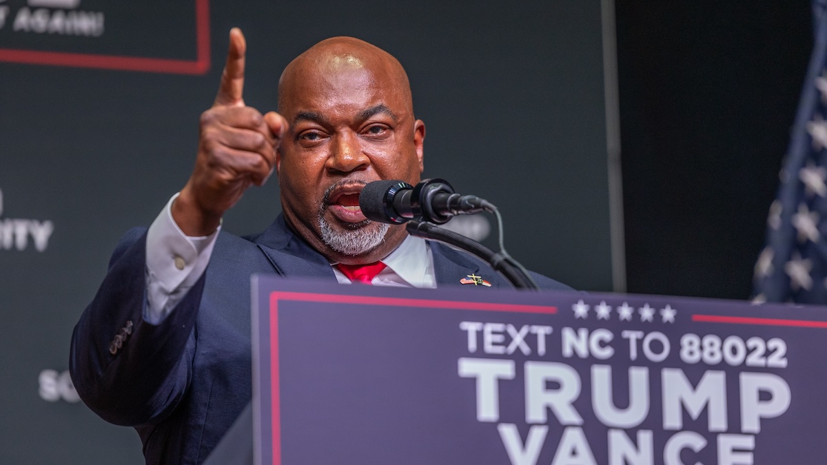 Mark Robinson gesturing emphatically while speaking at a Trump/Vance branded podium.