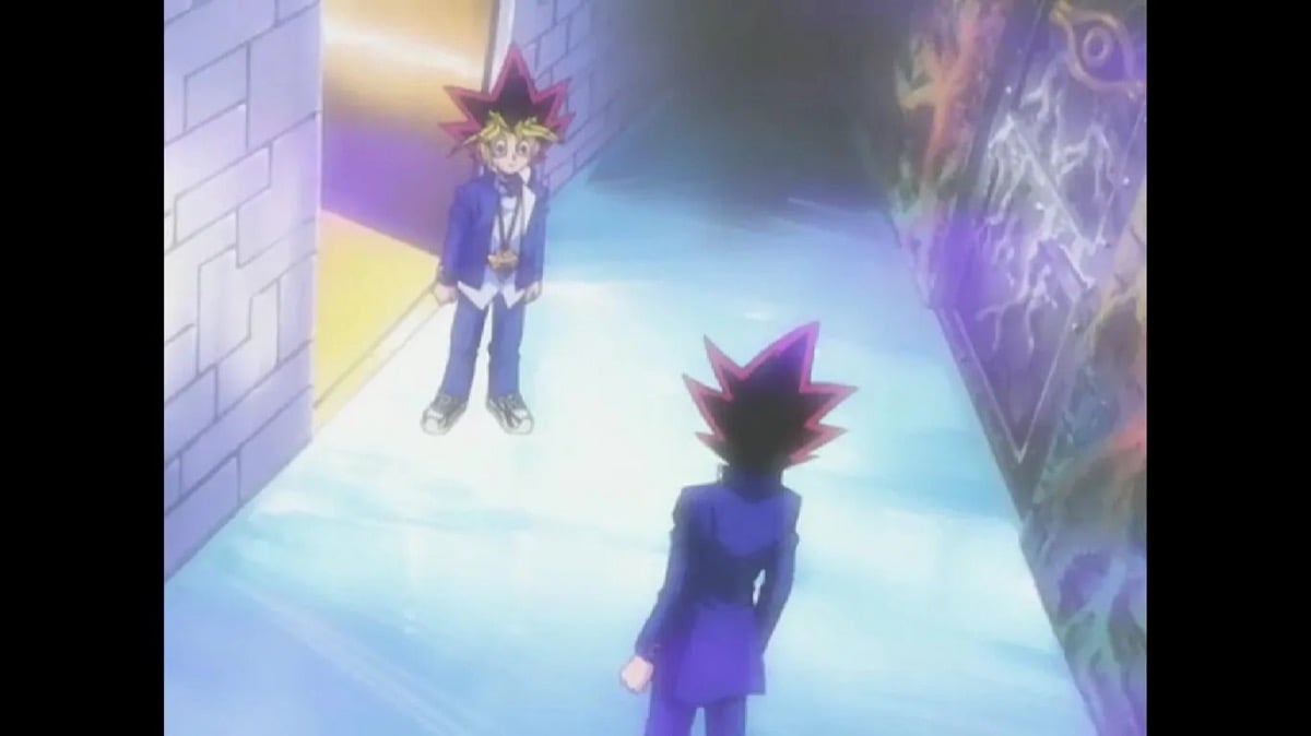 A man man stands in a hallway looking at a reflection of himself in  "Yu Gi Oh!"