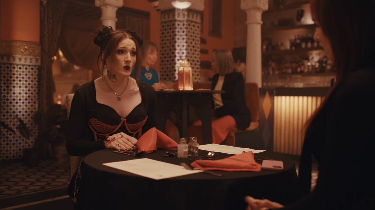 Dracula's ex girlfriend sitting at a table with a drink