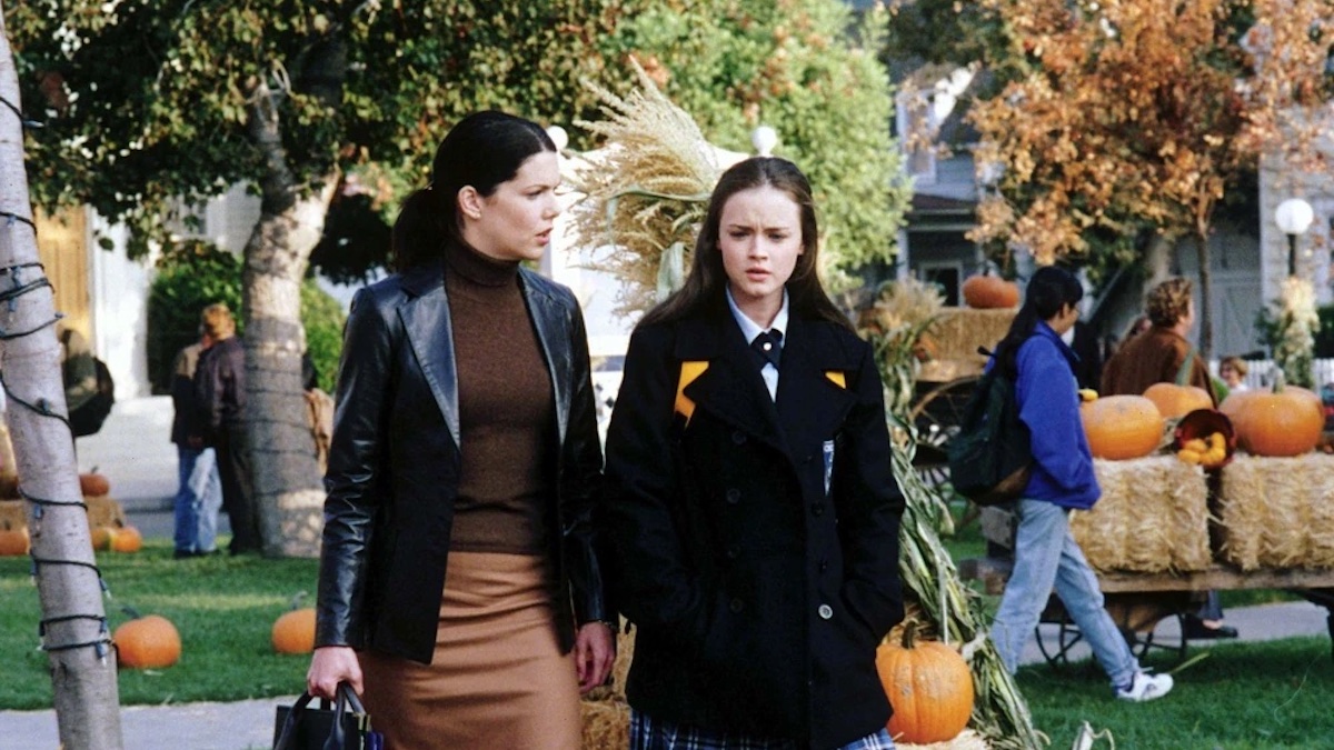 A still from Gilmore Girls season 1, episode 7 "Kiss and Tell," as Rory and Lorelai walk through Stars Hollow during the fall