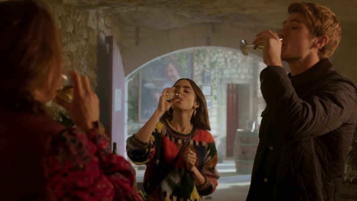 Emily (Lily Collins) downs a glass of wine as two others do the same in Emily In Paris