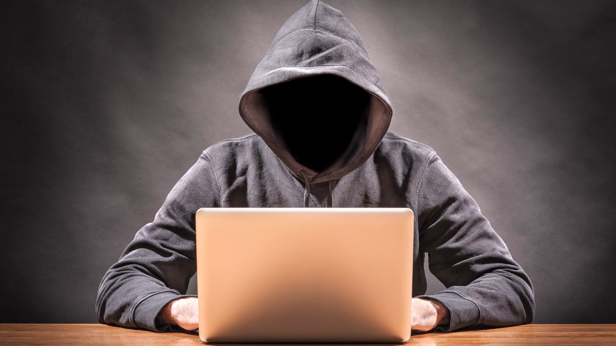 A faceless man in a hoodie looking at a computer ominously