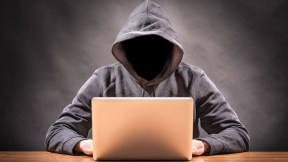 A faceless man in a hoodie looking at a computer ominously