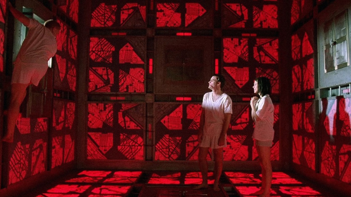 A still from the 'Cube' with two people standing inside a giant red cube