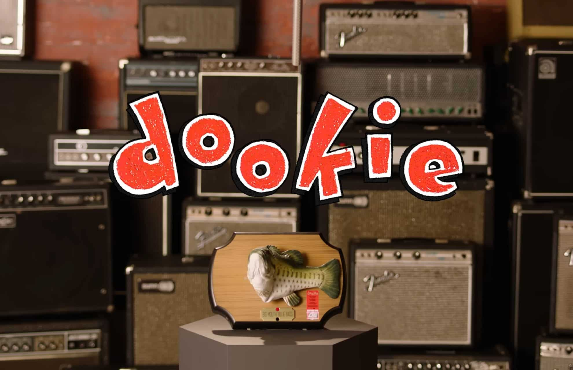 The word "dookie" in a playful, red font with a cartoonish style, placed over a background of vintage guitar amplifiers, with a mounted Big Mouth Billie Bass at the bottom center.