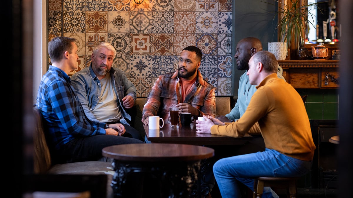 Three-quarter-length shot of five male friends having hot drinks in a rustic bar. They are having a serious conversation all wearing casual clothing. The bar/restaurant is located in Hexham.