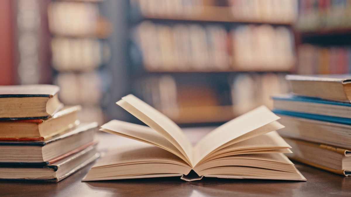 Library, books on table and background for studying, learning and research in education, school or college. Reading, philosophy and open, vintage or history print book, university blurred background