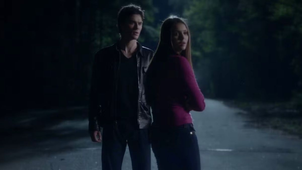 Damon and Elena stand in the middle of the road while she looks back in The Vampire Diaries