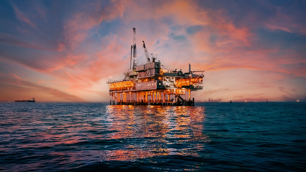 A stunning sunset photo showcases offshore oil drilling in Huntington Beach, California, with vivid hues casting a glow on industrial equipment