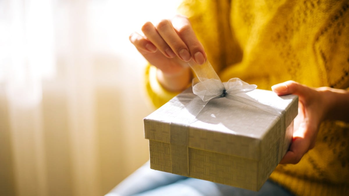 A person unties a bow on a brown gift box