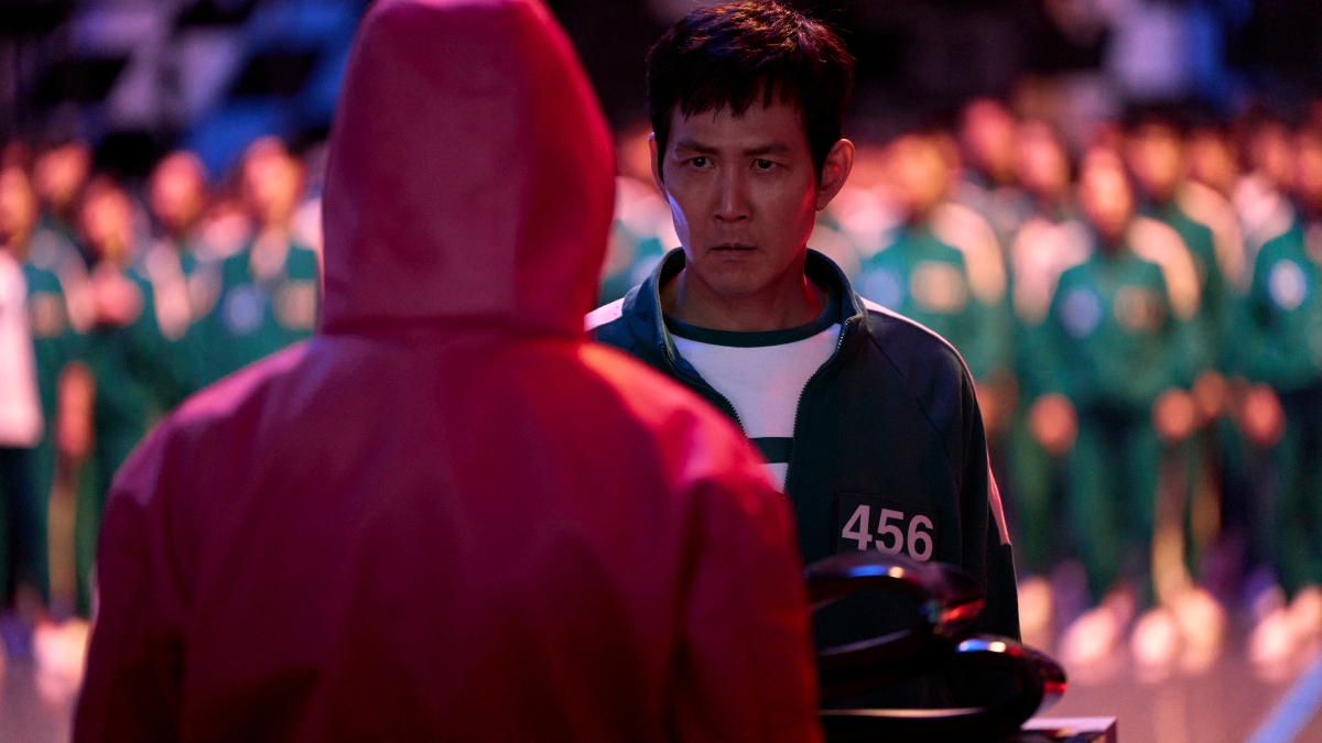 A still from 'Squid Game 2' featuring Seong Gi Hun (played by Lee Jung Jae) facing a guard from the Games, with a crowd of other players behind him