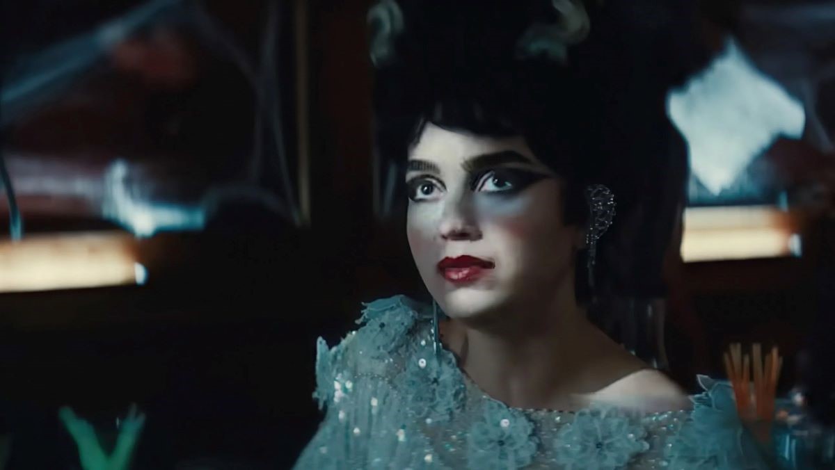 Image of Melissa Barrera in a scene from the film 'Your Monster.' She is a Latina with dark hair wearing a sequined floral dress costume with sparkly earrings and dramatic theatrical make-up.