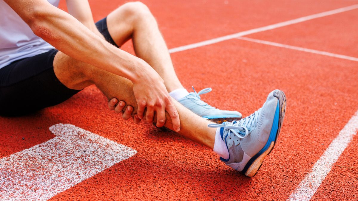 Athlete holding his leg injured after running at track and field stadium after jogging, running competition, sports injury concept