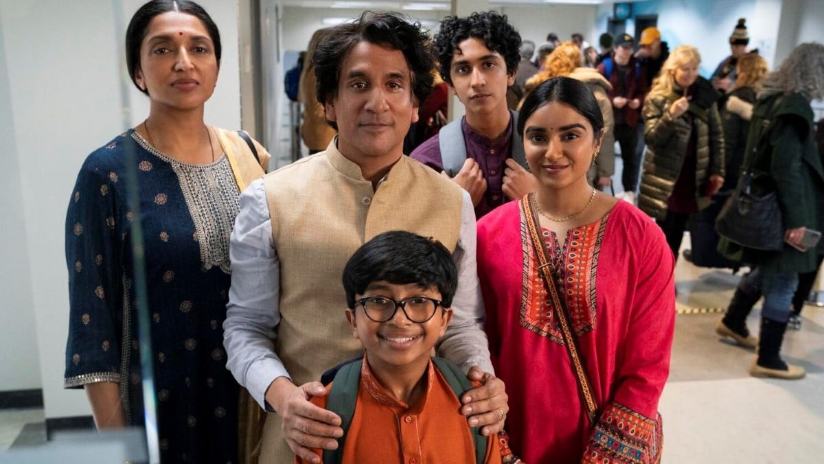 Image of the Pradeep family (actor Naveen Andrews, center) in a scene from Prime Video's 'The Pradeeps of Pittsburgh.' They are an Indian family standing smiling for a photo in an airport: Father in the middle with his hands on his youngest son's shoulders. Mother stands to the father's right, his teen daughter is on his left, and his teen son stands behind them looking not thrilled to be there.