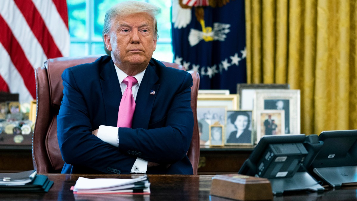 Donald Trump crosses his arms while sitting at a desk in the Oval Office