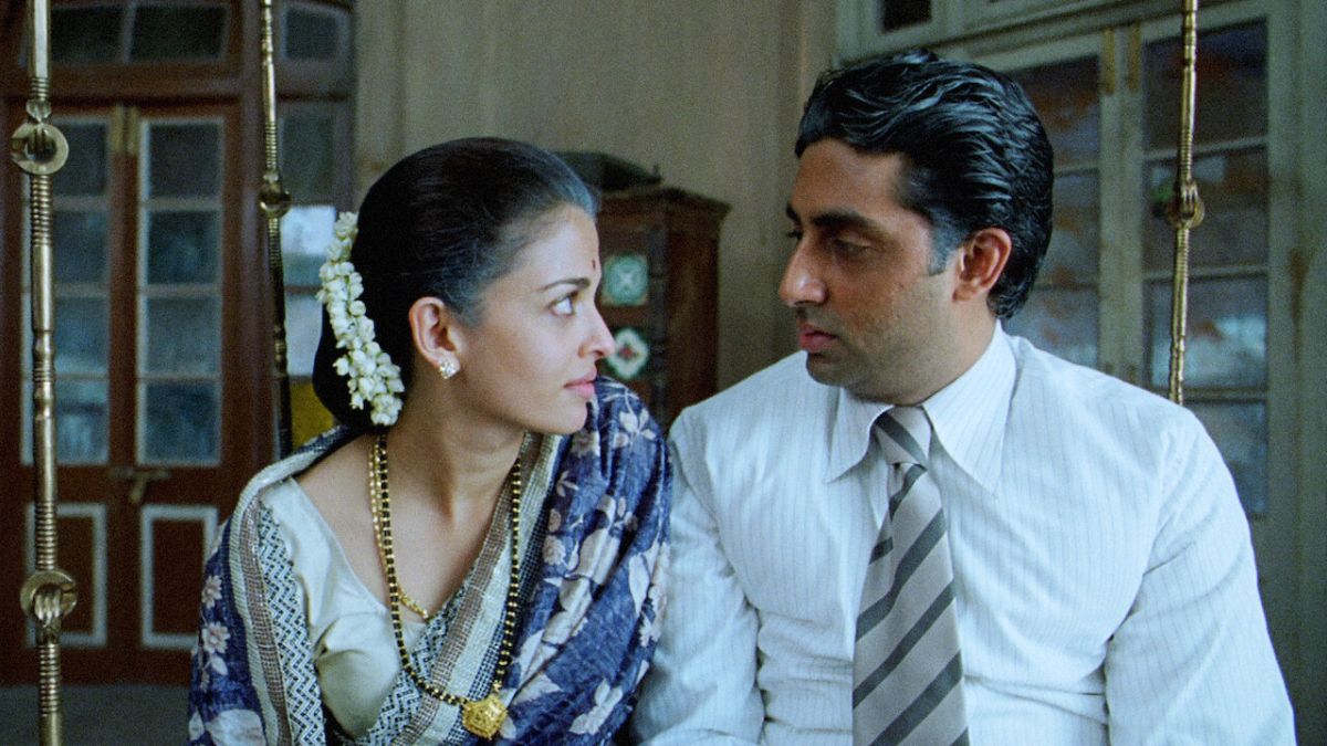 An aged Indian woman and man sit on a swing, looking at each other