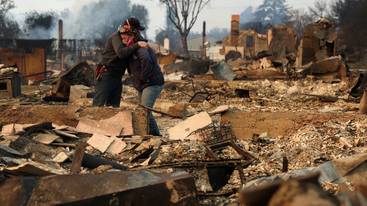 Two people hug while surveying the devestation of the California wildfires