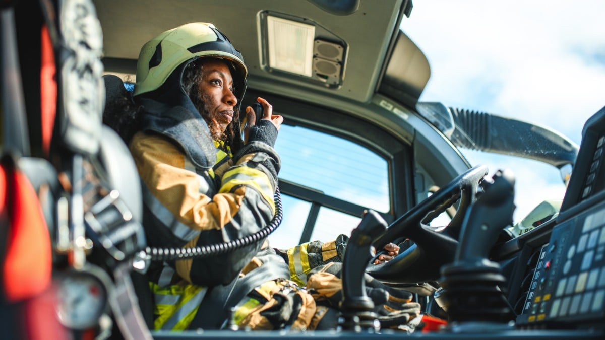 A female firefighter talks into a speaker while driving a fire truck