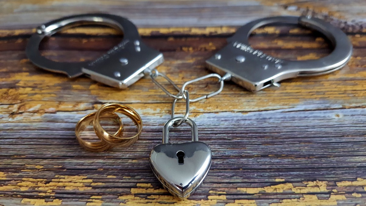 Wedding rings sit next to handcuffs with a heart-shaped lock