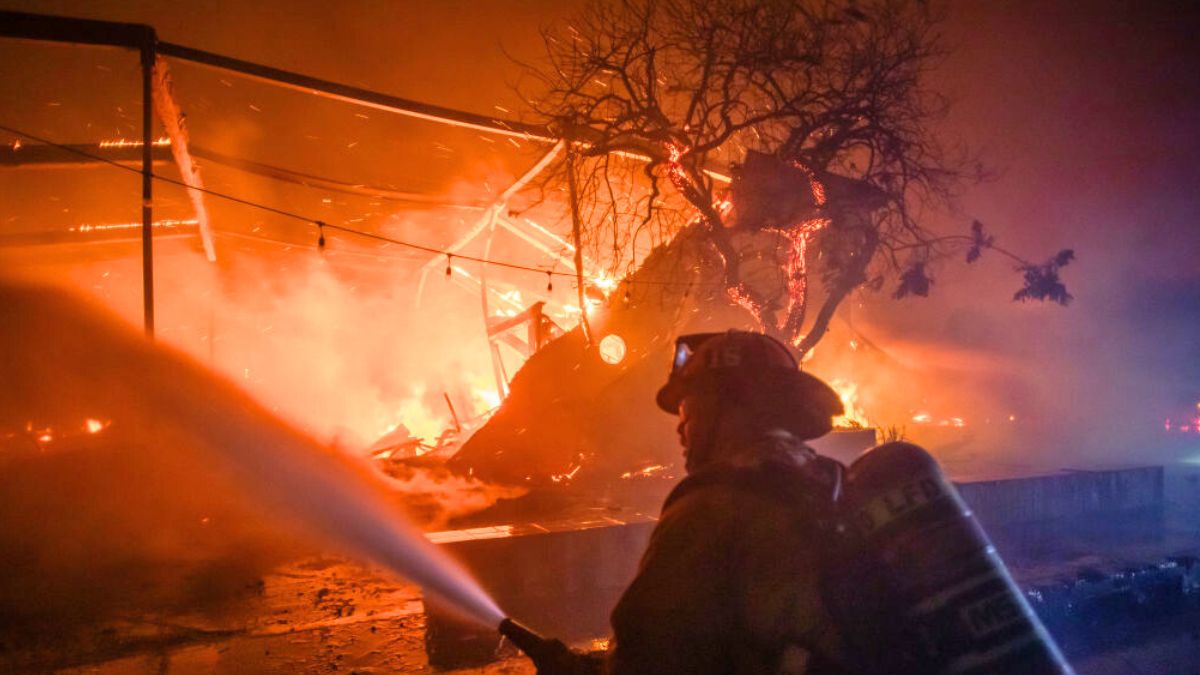 LOS ANGELES, CALIFORNIA - JANUARY 8: A Firefighter fights the flames from the Palisades Fire burning the Theatre Palisades during a powerful windstorm on January 8, 2025 in the Pacific Palisades neighborhood of Los Angeles, California. The fast-moving wildfire is threatening homes in the coastal neighborhood amid intense Santa Ana Winds and dry conditions in Southern California. (Photo by Apu Gomes/Getty Images)