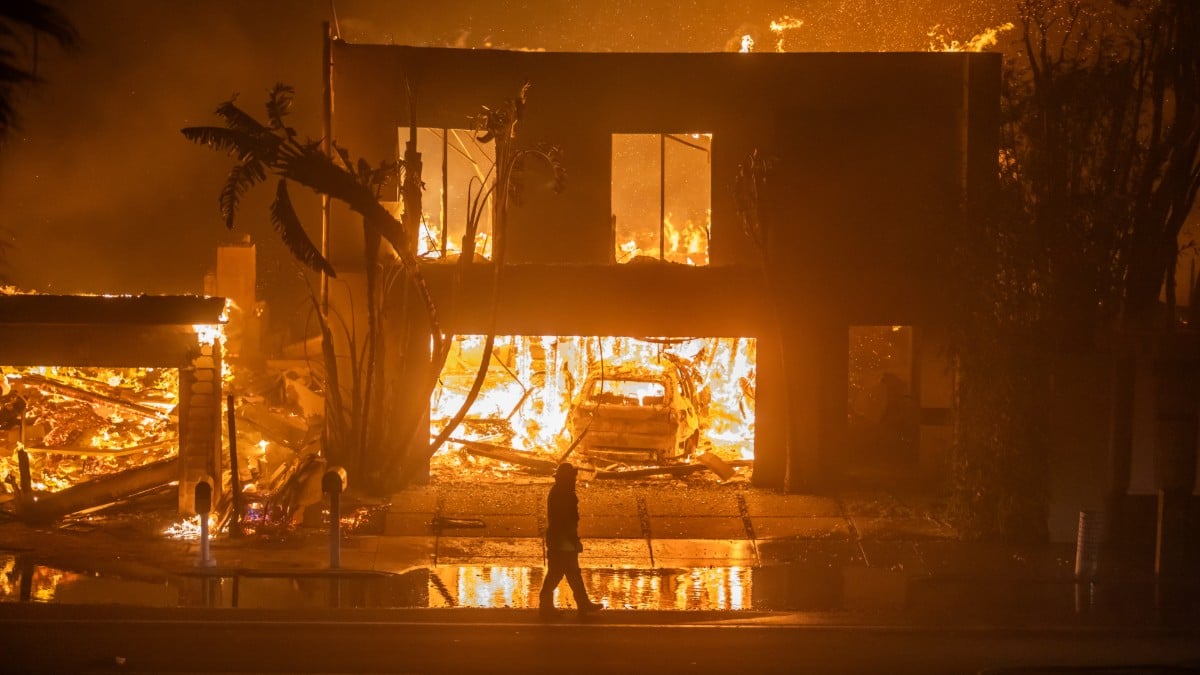 A firefighter watches a house in LA burn from the Palisades Fire