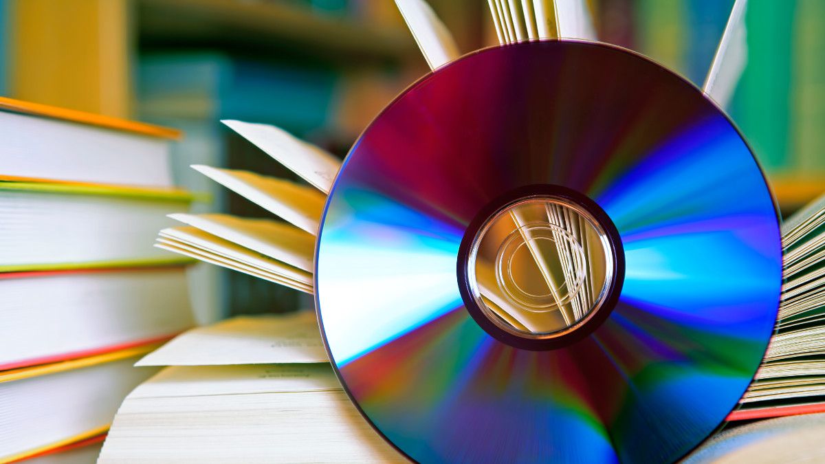 A DSLR photo of an open book with a CD in front of it. Some other books are visible at the background. Shallow depth of field.