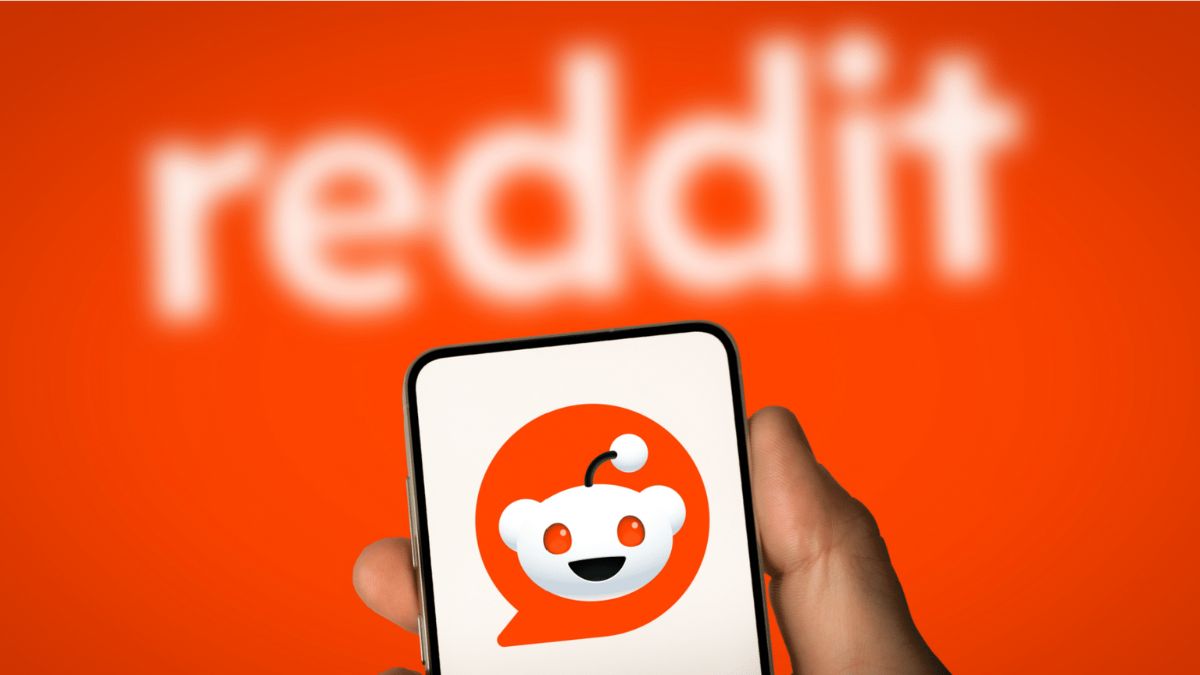 An picture of a smartphone with the Reddit logo on the screen, in front of an orange background.