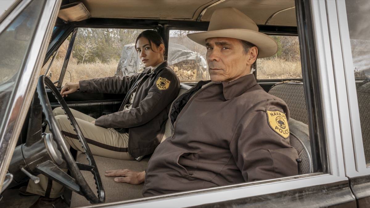 Two Navajo police officers peer out the window of their squad car in "Dark Winds"