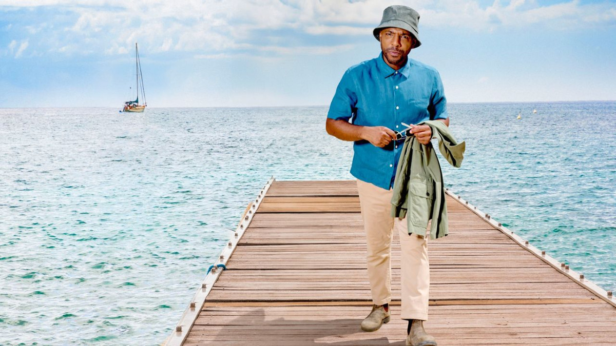 Don Gilet walking down a boardwalk as Death in Paradise's DI Mervin Wilson