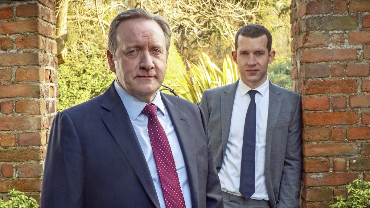 Two men in suits stand in woodland architecture and stare into the camera in "Midsomer Murders"