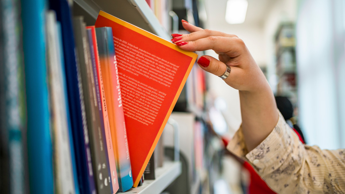 Woman's hand picking a book from a library bookshelf - stock photo